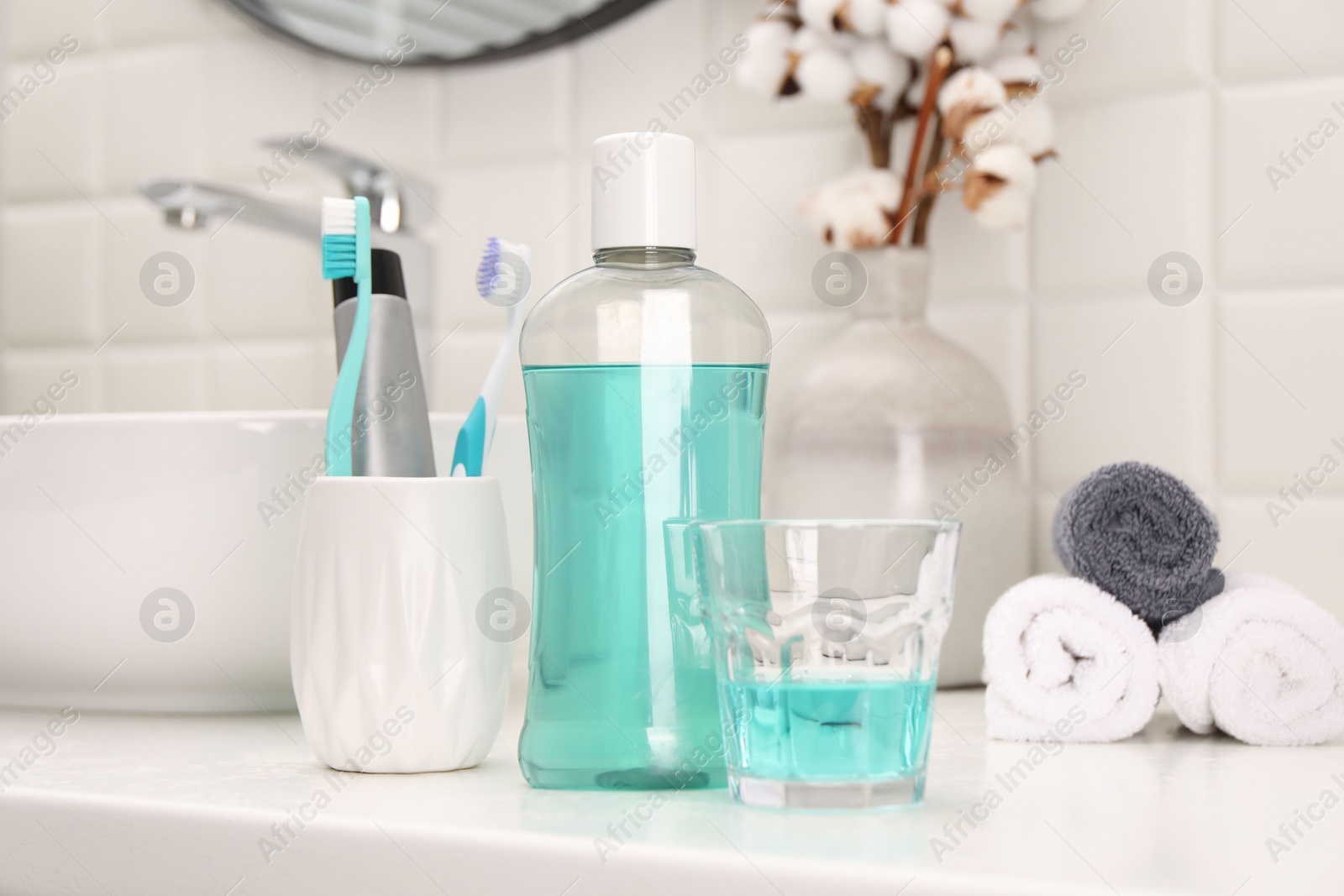 Photo of Bottle of mouthwash and glass on white table in bathroom