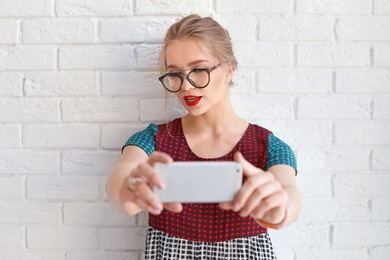 Photo of Attractive young woman taking selfie near brick wall