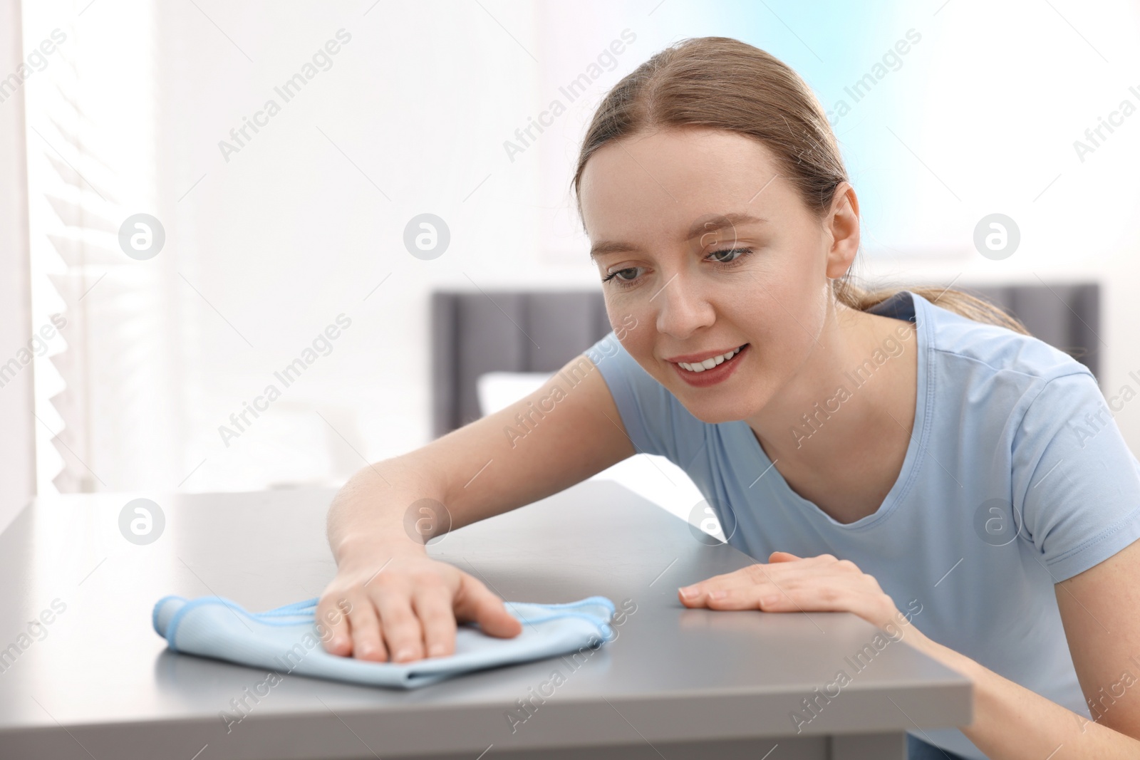 Photo of Woman with microfiber cloth cleaning grey chest of drawers in room