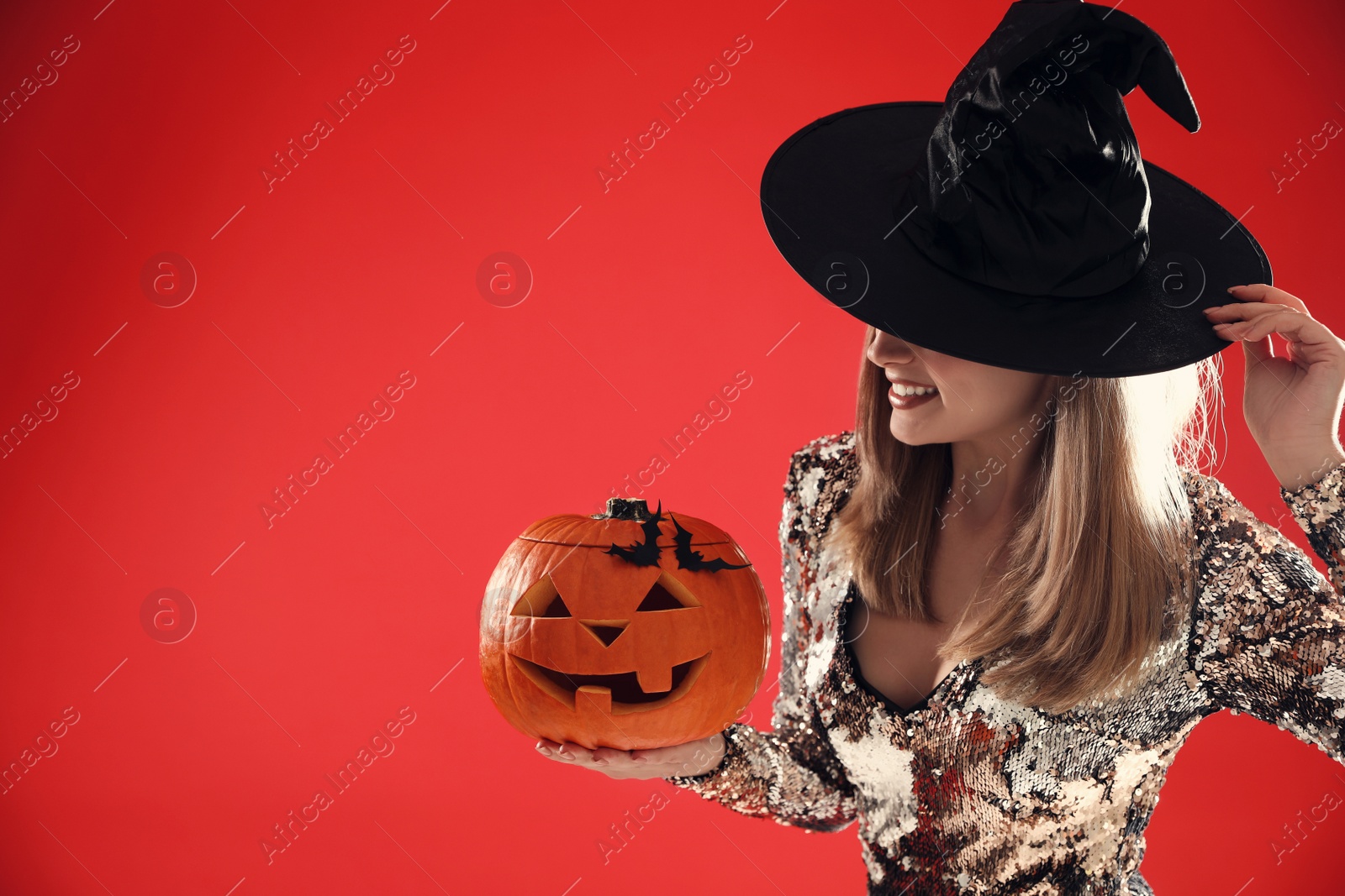 Photo of Beautiful woman in witch costume with jack o'lantern on red background, space for text. Halloween party