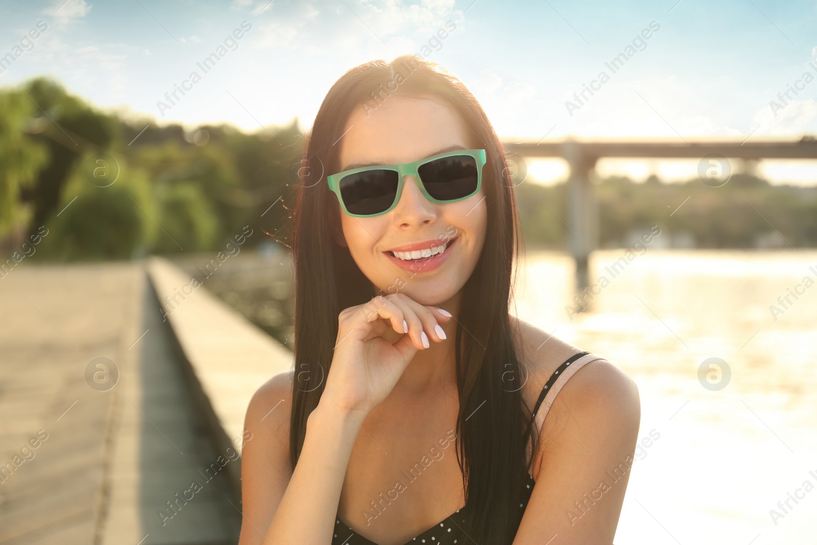 Photo of Beautiful young woman wearing stylish sunglasses near river