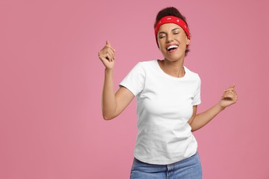 Photo of Happy young woman in stylish headband dancing on pink background. Space for text