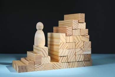 Photo of Stairs of blocks with gap as barrier and wooden human figure on light blue surface. Path to growth and success
