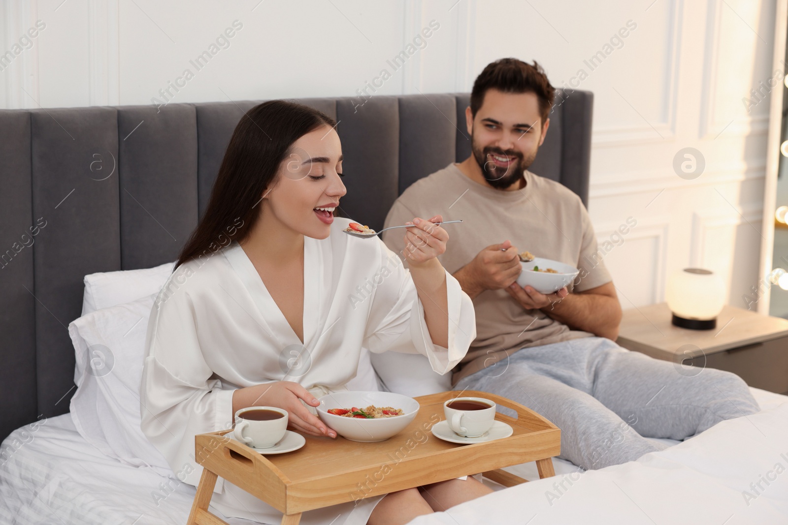 Photo of Happy couple having breakfast on bed at home