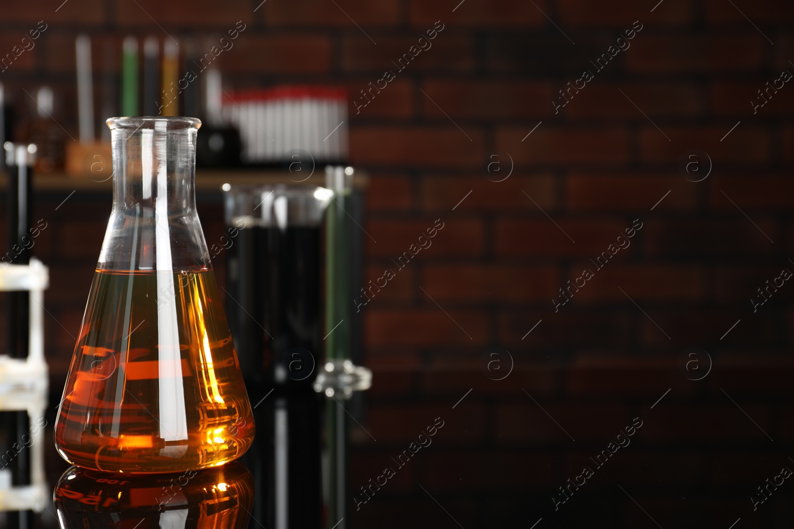 Photo of Laboratory glassware with different types of oil on black mirror table indoors, closeup. Space for text