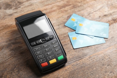 Photo of Modern payment terminal and credit cards on wooden background