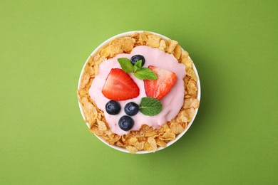Photo of Delicious crispy cornflakes, yogurt and fresh berries in bowl on green background, top view. Healthy breakfast