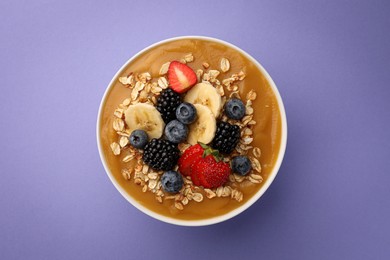 Delicious smoothie bowl with fresh berries, banana and oatmeal on violet background, top view