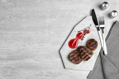 Photo of Stone board with grilled meat and sauce on light background, top view. Space for text