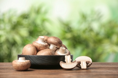Photo of Plate of fresh champignon mushrooms on wooden table against blurred background