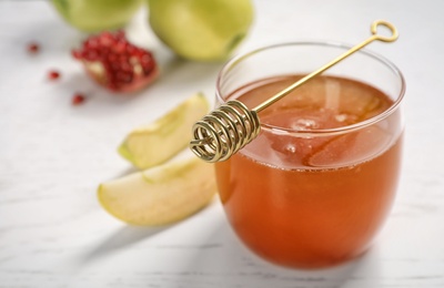 Photo of Glass of honey, apples, pomegranate and dipper on light table. Rosh Hashanah holiday