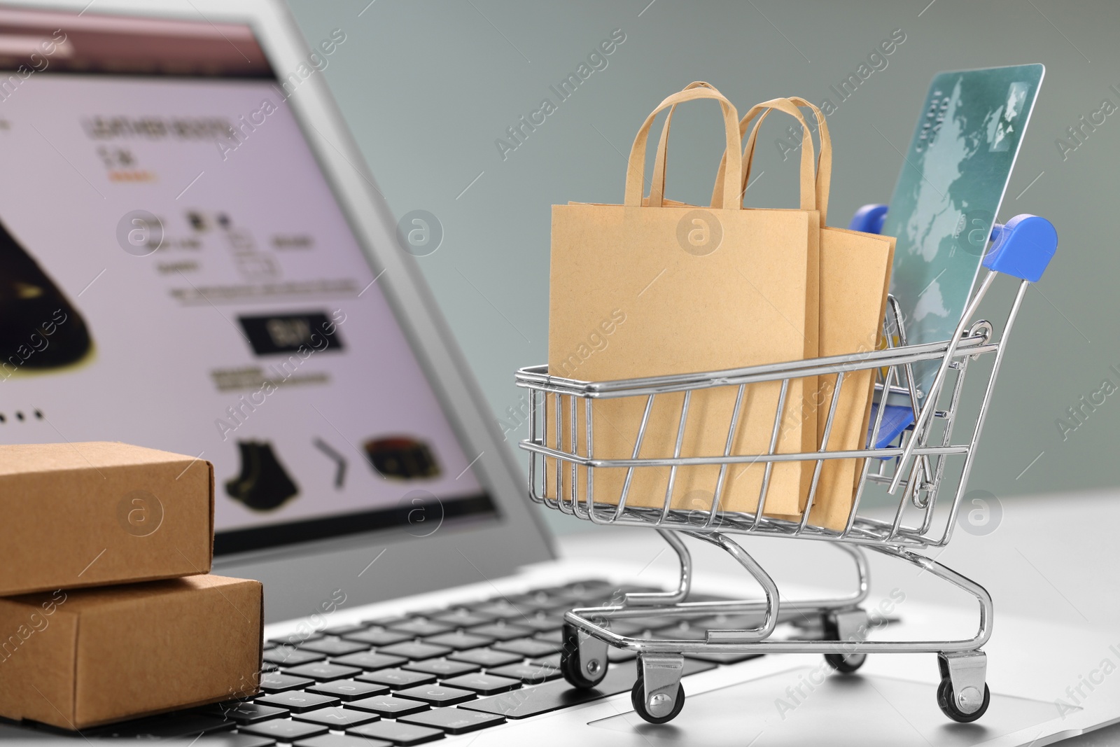 Photo of Mini shopping bags, credit card, cart and boxes on laptop against light grey background, closeup. Online store