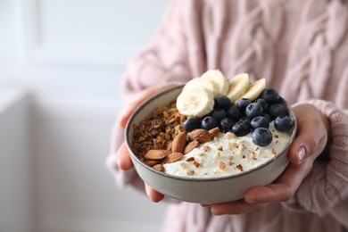 Photo of Woman holding bowl of tasty granola indoors, closeup. Space for text