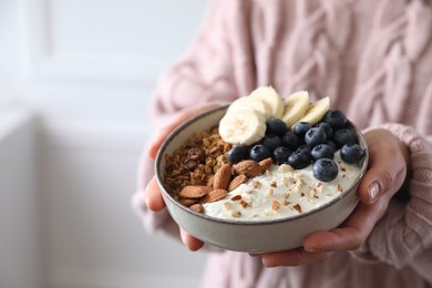 Woman holding bowl of tasty granola indoors, closeup. Space for text