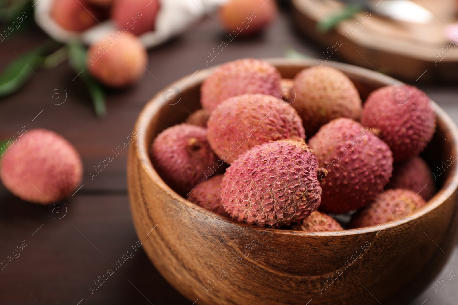 Photo of Fresh ripe lychee fruits in bowl on wooden table, closeup