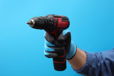 Photo of Handyman holding electric screwdriver on light blue background, closeup