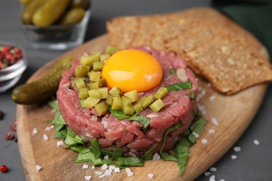 Photo of Tasty beef steak tartare served with yolk, pickled cucumber and other accompaniments on grey table, closeup