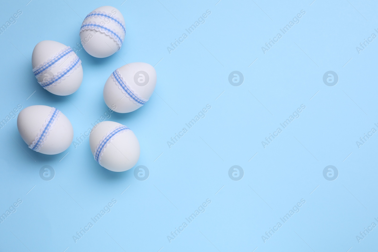Photo of Beautifully decorated Easter eggs on light blue background, flat lay. Space for text