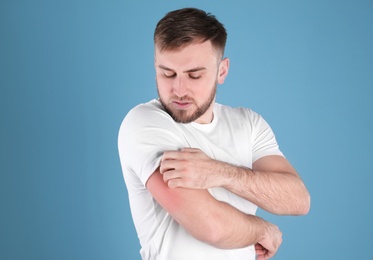 Photo of Man scratching arm on color background. Allergy symptoms