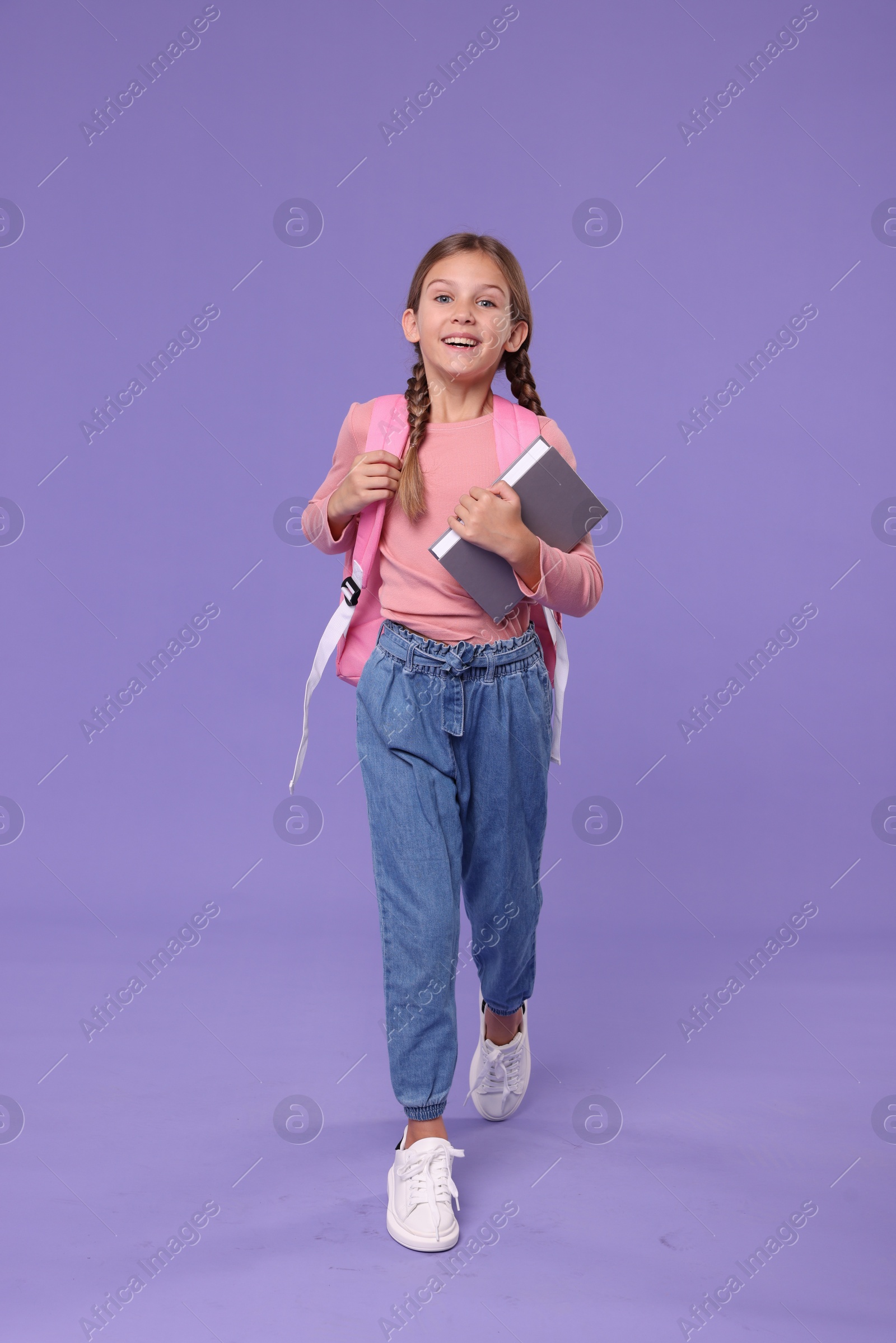 Photo of Happy schoolgirl with books on violet background