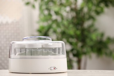 Photo of Modern yogurt maker with empty jars on white table indoors. Space for text