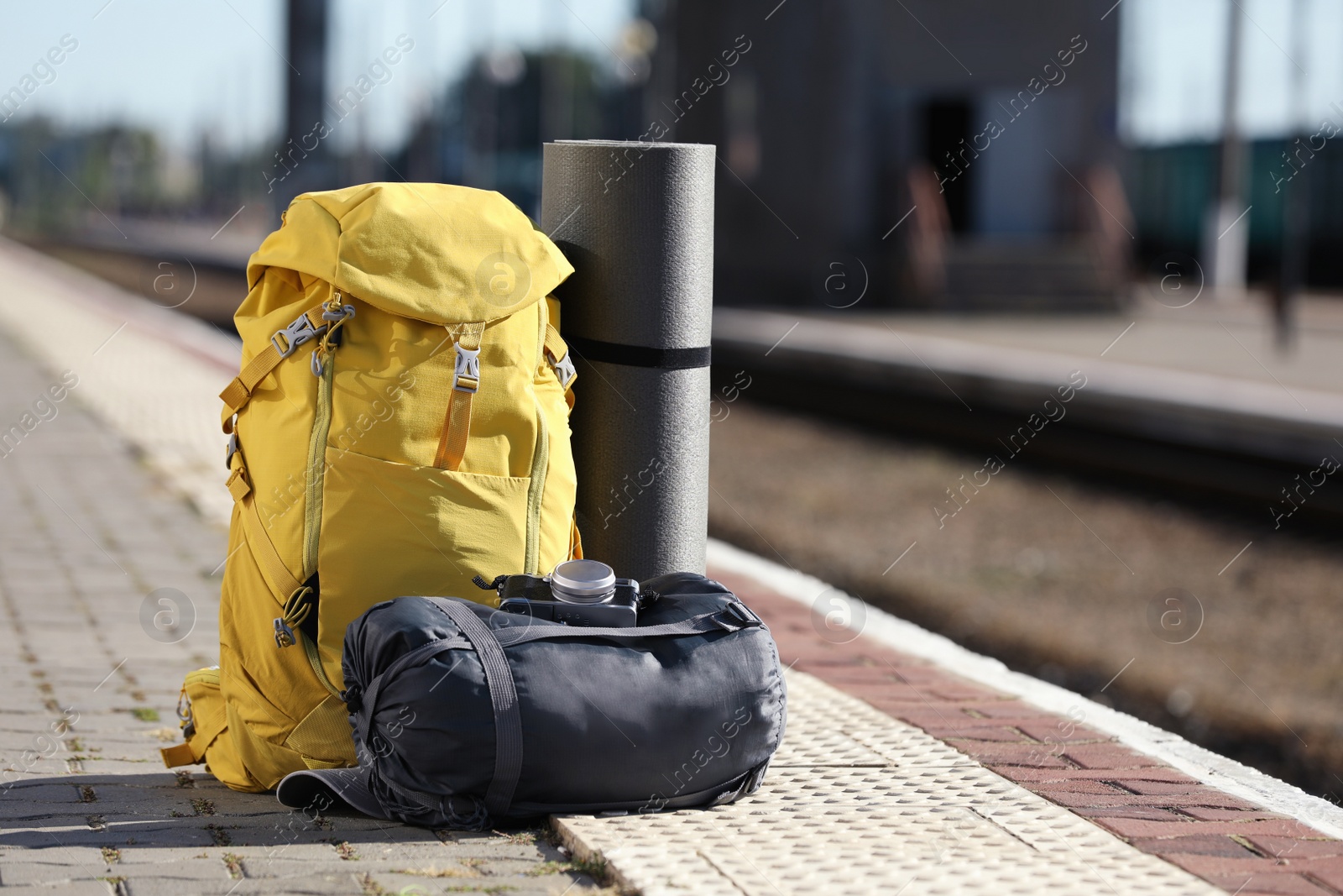 Photo of Stylish backpack, sleeping bag, camera and camping mat on railway platform outdoors. Tourism concept
