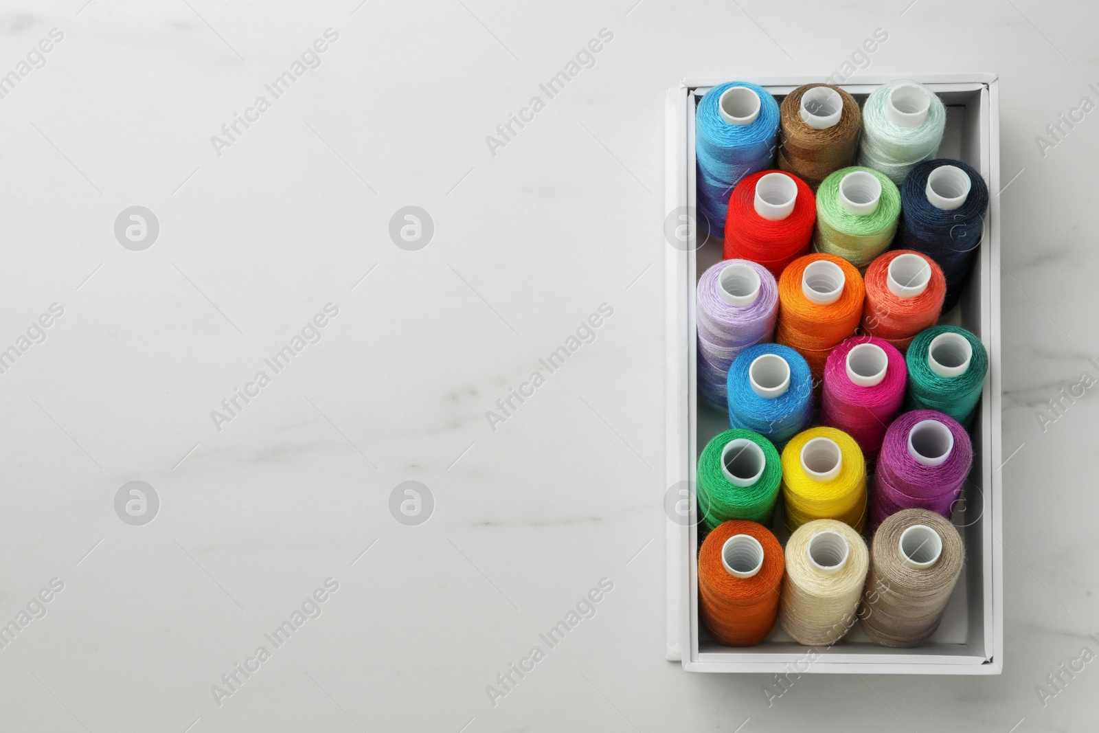 Photo of Box with colorful sewing threads on white marble table, top view. Space for text