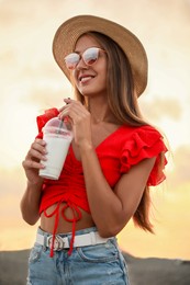 Beautiful young woman with tasty milk shake on beach