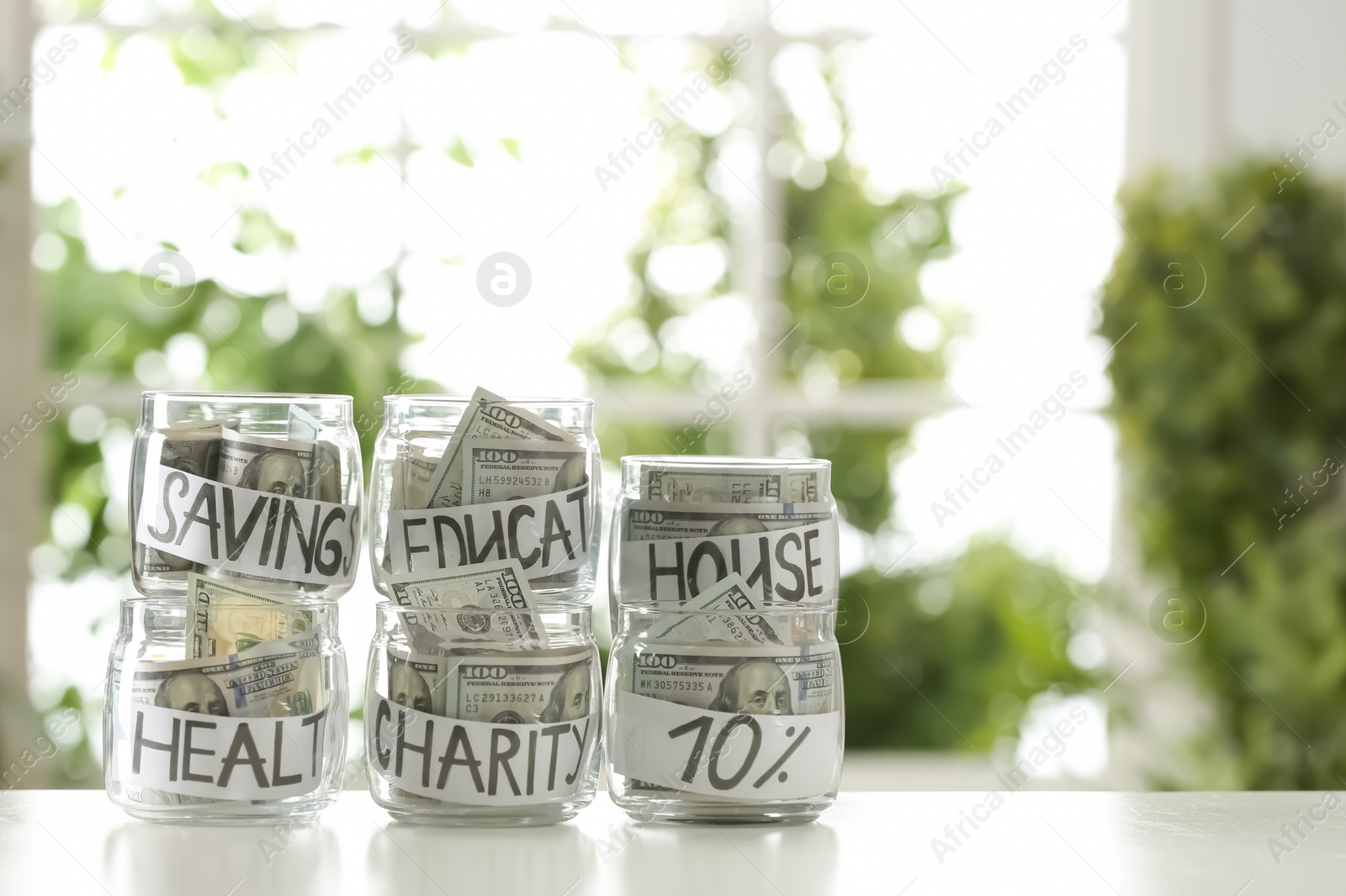 Photo of Glass jars with money for different needs on table against blurred background, space for text