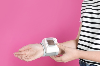 Young woman checking pulse with digital medical device on color background, closeup. Space for text