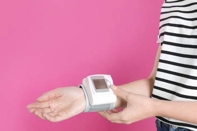 Photo of Young woman checking pulse with digital medical device on color background, closeup. Space for text