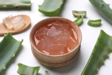 Aloe vera gel in bowl and slices of plant on white textured background, closeup