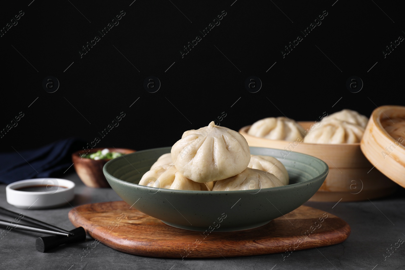 Photo of Delicious bao buns (baozi) in bowl on grey table, closeup