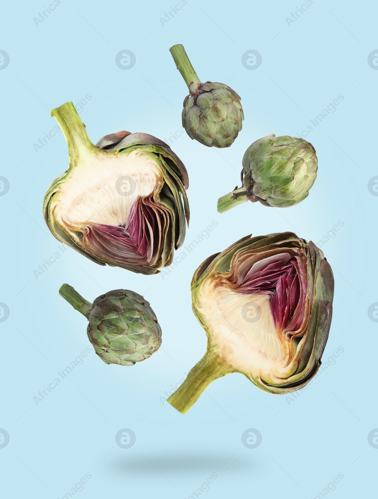 Image of Fresh raw artichokes falling on light blue background