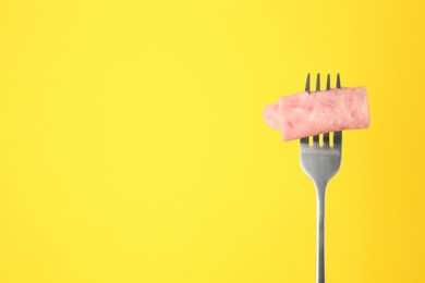 Photo of Fork with tasty slice of ham on yellow background, space for text