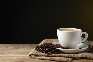 Cup of hot aromatic coffee and roasted beans on wooden table against dark background, space for text