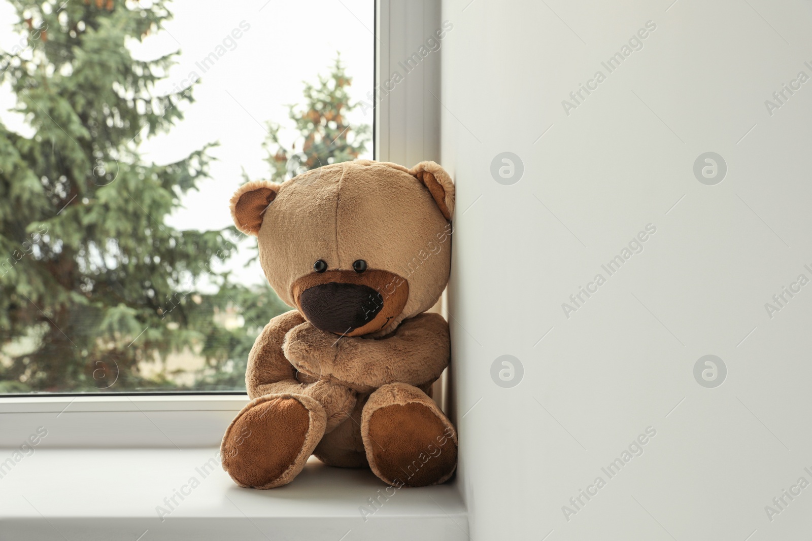 Photo of Cute lonely teddy bear on windowsill indoors. Space for text