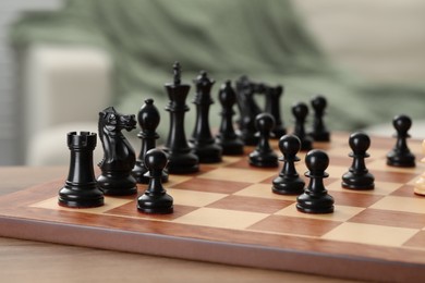 Chess board with black pieces on wooden table, closeup