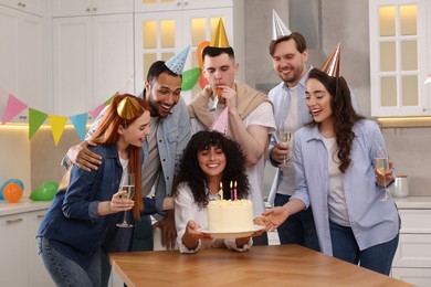 Photo of Happy friends with tasty cake celebrating birthday in kitchen
