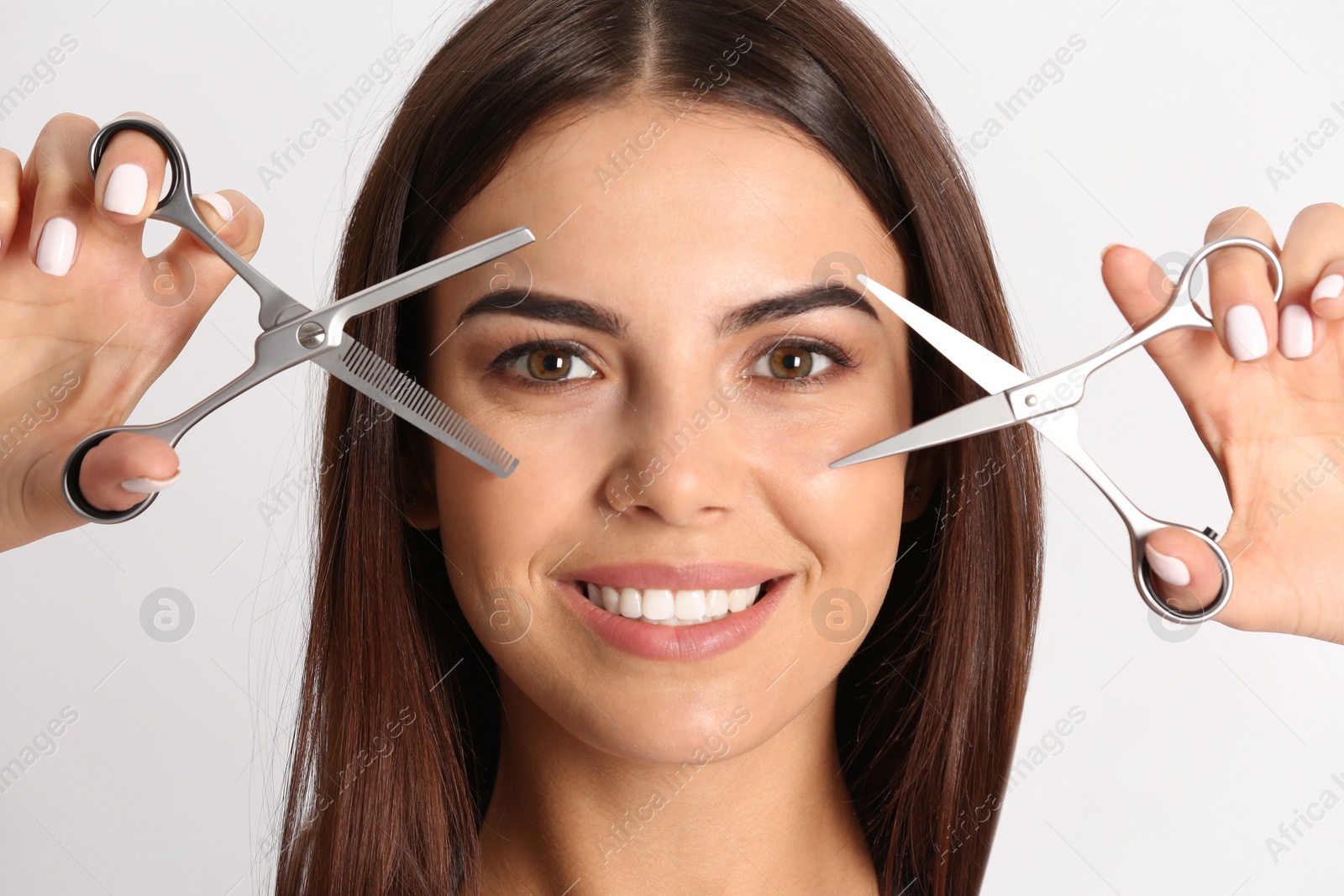 Photo of Young hairstylist holding professional scissors on light background, closeup