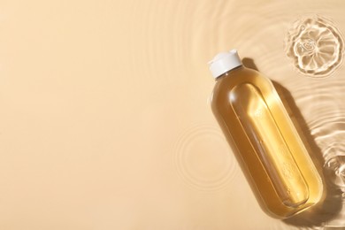 Photo of Wet bottle of micellar water on beige background, top view. Space for text