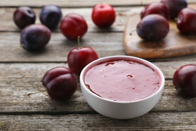 Plum puree in bowl and fresh fruits on wooden table