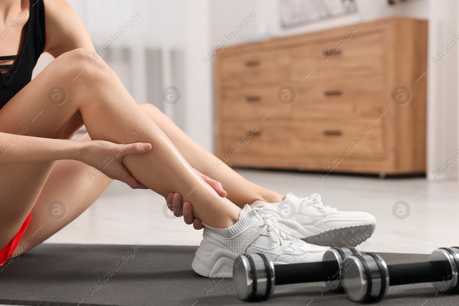 Photo of Woman suffering from leg pain on exercise mat in room, closeup