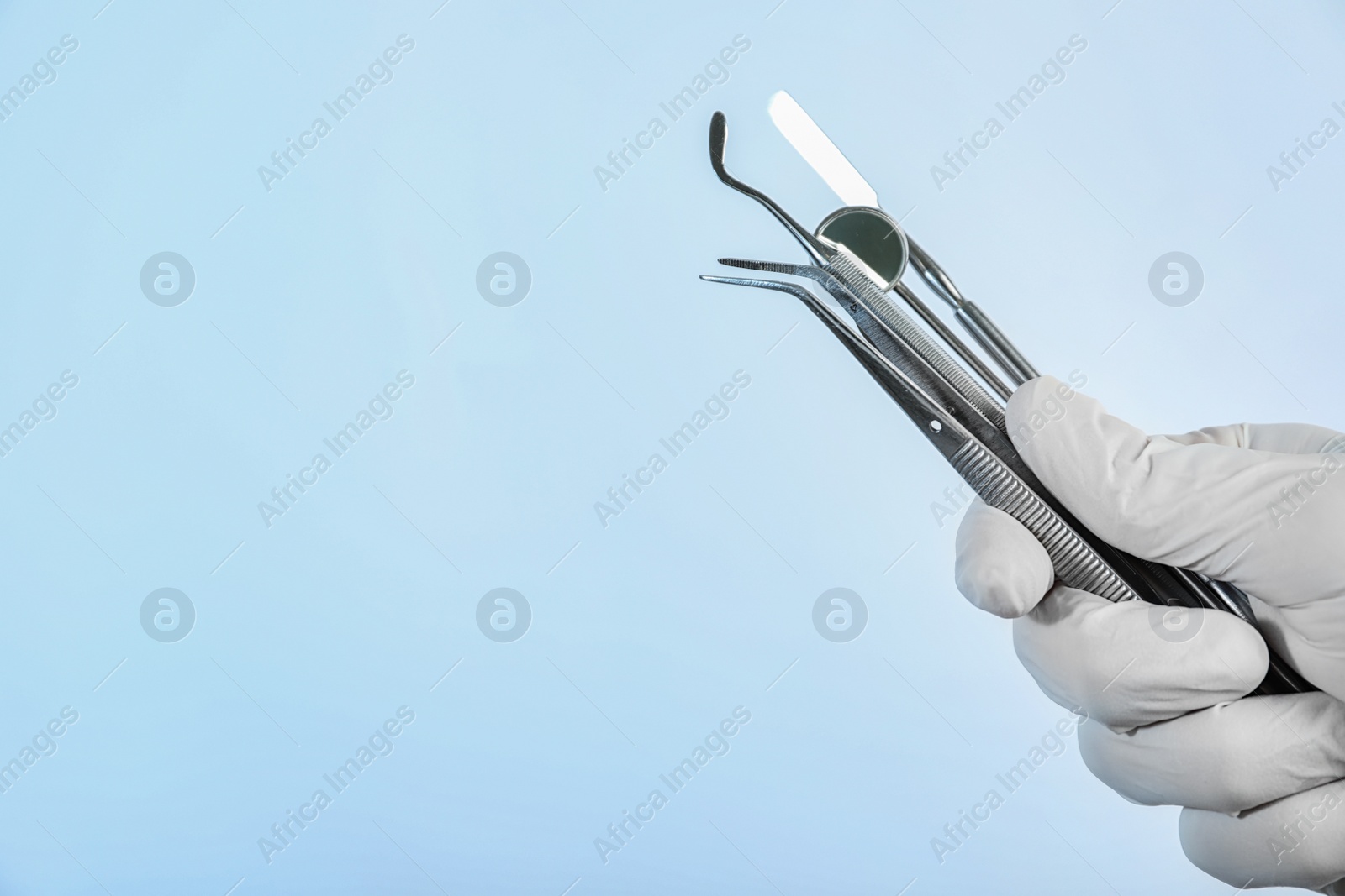 Photo of Dentist holding professional tools on light background, closeup. Space for text