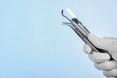 Photo of Dentist holding professional tools on light background, closeup. Space for text