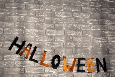 Photo of Word Halloween made of colorful letters on brick wall. Festive decor