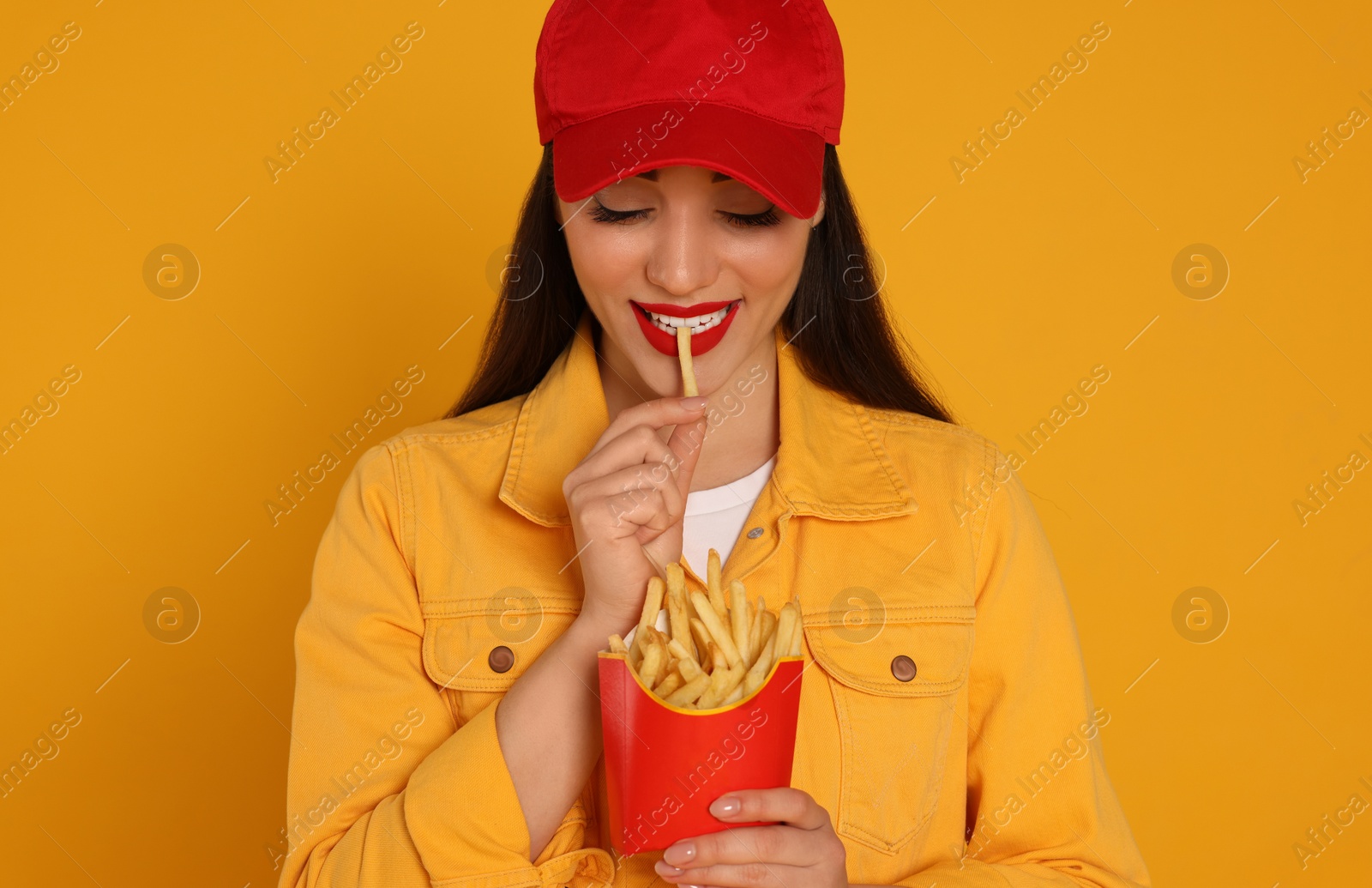 Photo of Beautiful young woman eating French fries on yellow background