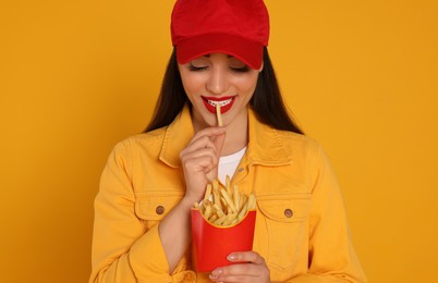 Beautiful young woman eating French fries on yellow background