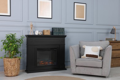 Black stylish fireplace near armchair and potted plant in cosy living room