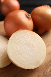 Whole and cut yellow onions on wooden table, closeup